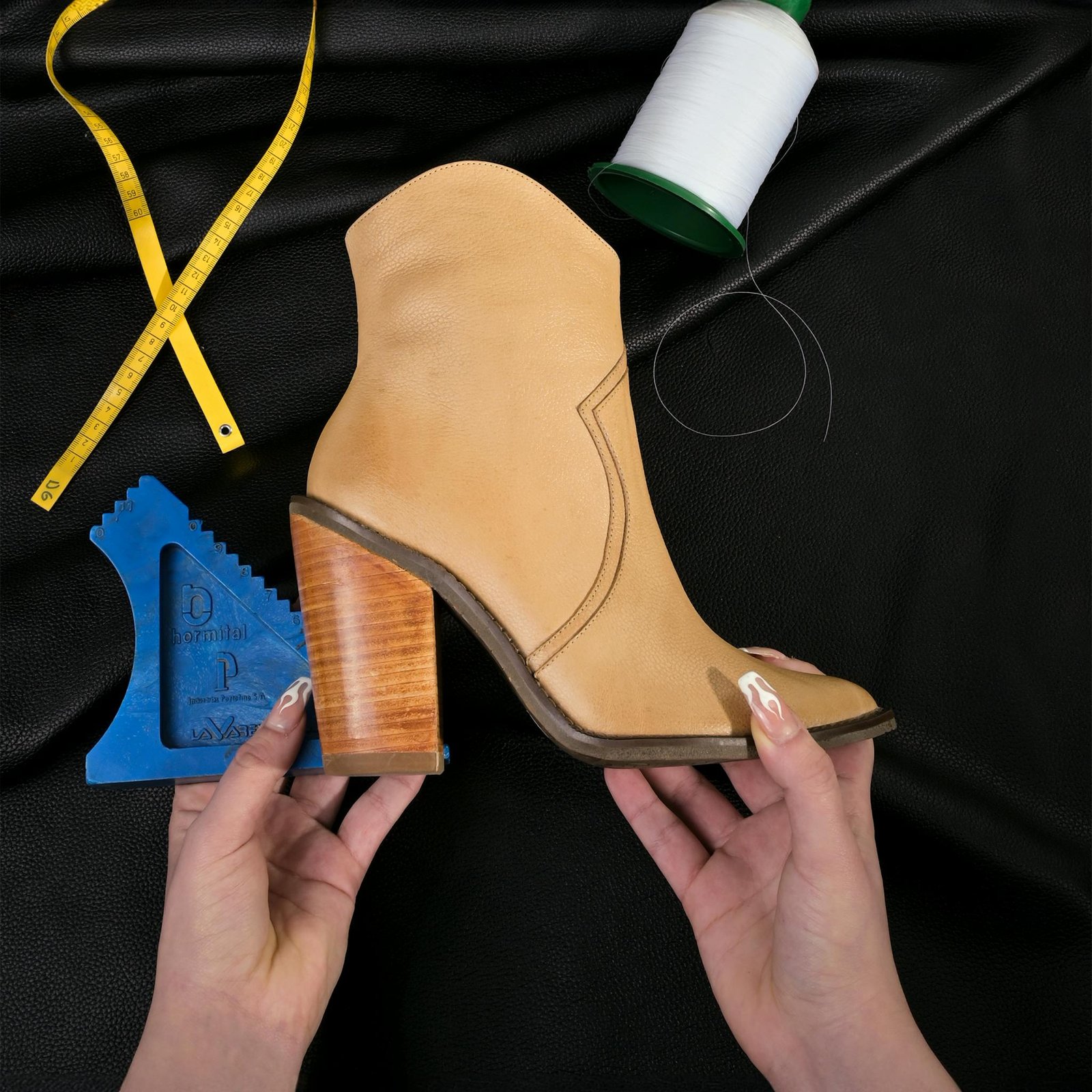 A handmade leather boot is held, surrounded by sewing tools. Ideal for fashion and craft themes.