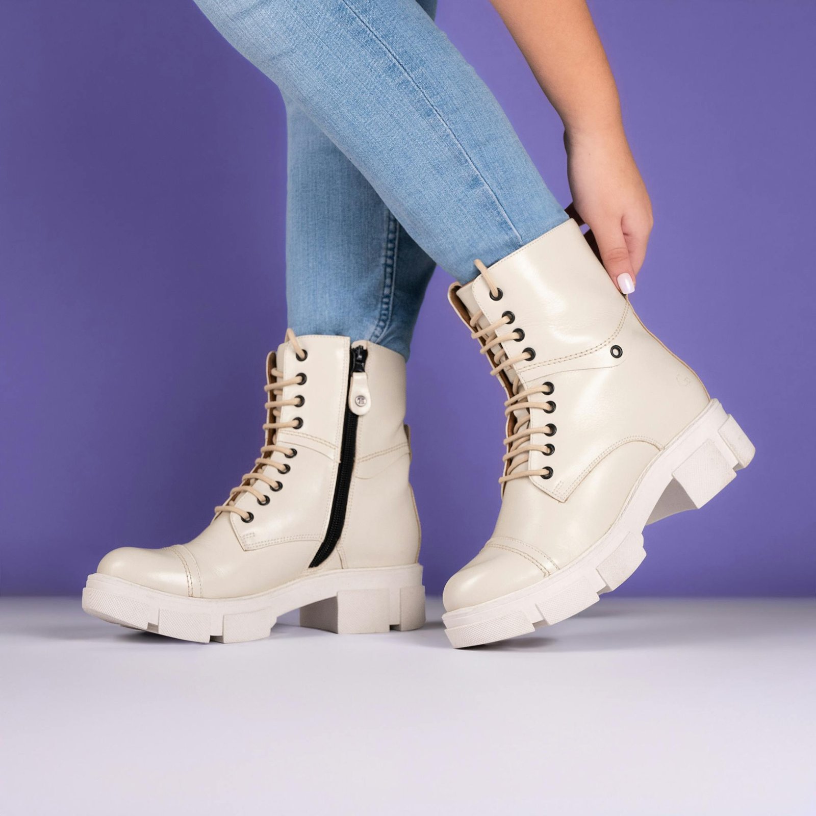 Elegant beige boots paired with jeans against a lilac background.