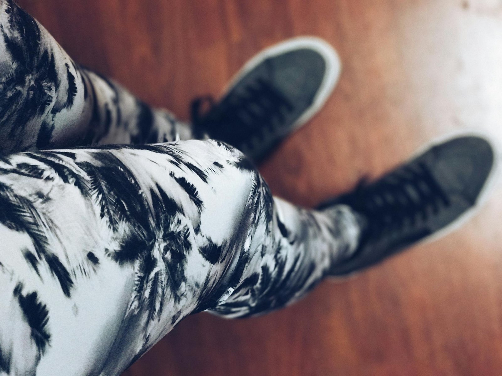 High-angle view of trendy sneakers paired with abstract patterned leggings on wooden flooring.